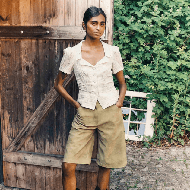 Model in Baum Und Pferdgarten Macaia Blouse and Numa shorts in front of barn door