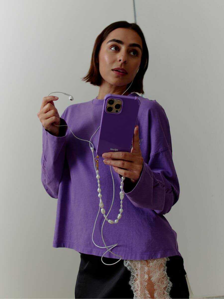 Atelje Balance Short Cord with Phone case in violet held by model wearing purple long sleeve tee and black silk skirt with cream lace side slit