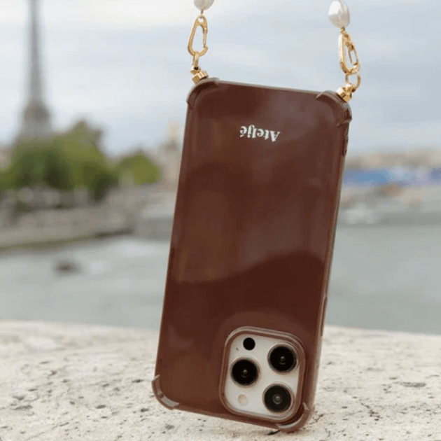 Atelje Dark Brown Phone Case hanging from pearl cord resting against bridge in Paris