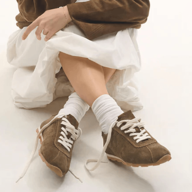 Bukela brown trainers worn with white socks, white maxi skirt and brown suede jacket