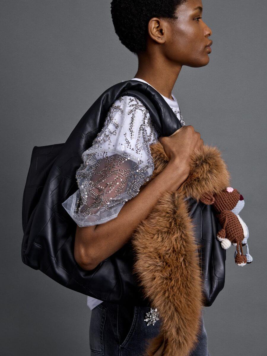 Munthe - Voida Collar tied around black leather slouchy bag with Vamke and Vallate crochet animal bag charms, worn with sheer glitter tee layered over graphic tee