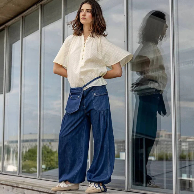 Model in front of glass wall wearing project AJ cream blouse and Denim wide leg pants