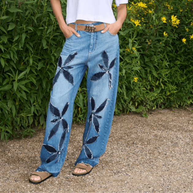 Model wearing Munthe Bimo jeans, camel suede belt, white tee and camel suede sandals in front of a flowery hedge